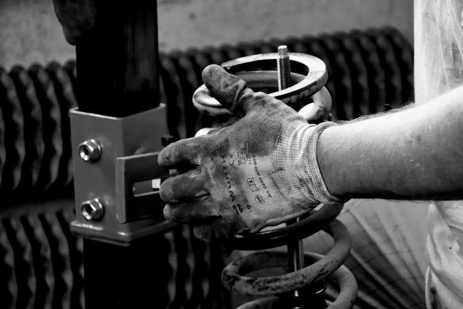 Close-up of a gloved auto mechanic's hand working with a spring in a workshop.